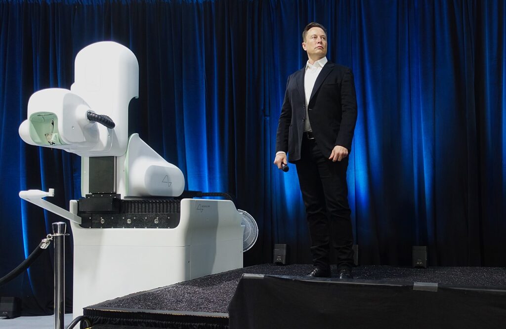 Elon musk se tient derrière un robot chirurgical, sur une scène